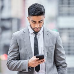 Shot of a young businessman using his smartphone while walking outside.